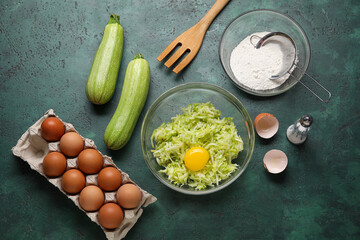 Bowls with grated zucchini, flour and eggs for preparing fritters on green background