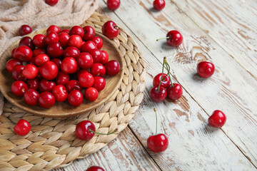 Plate with sweet cherries on white wooden background
