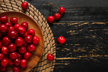 Plate with sweet cherries on black wooden background