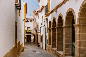 A picturesque view of a traditional alley in the old town of Javea, Valencia, adorned with Spanish architecture and arched doorways.