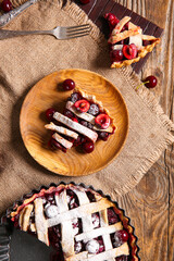 Baking dish with tasty cherry pie and plate of piece on wooden background