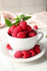 Cup with fresh raspberries and mint on white tile background