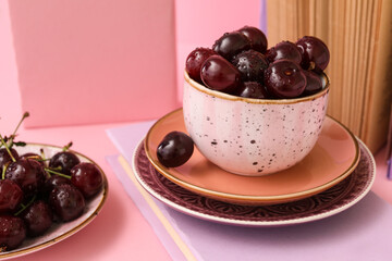 Cup and plate of sweet cherries with books on pink background