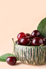Bowl with sweet cherries and leaves on beige background