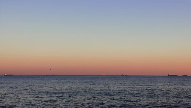 Sunset over calm sea, ships on roadstead bask in sunset glow. Tranquil sea waves at sunset, ships anchored in roadstead. Roadstead ships illuminated by sunset, calm sea waves