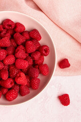 Bowl with fresh raspberries on pink background