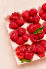 Ice cube tray with fresh raspberries and mint on light background