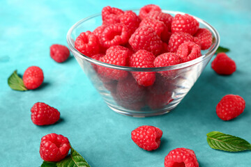 Glass bowl with fresh raspberries and mint on blue background