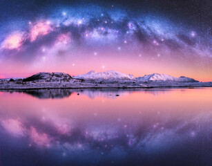 Milky Way arch over snowy mountains and sea coast at winter night. Landscape with snowy rocks, pink...