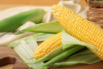 Wooden board with fresh corn cobs on brown background, closeup