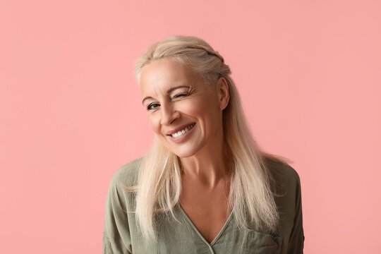 Mature woman winking on pink background, closeup