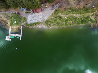 Drone view of a mountain lake with a pontoon with parked boats and a boat returning to the shore
