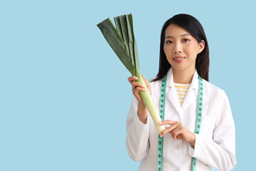 Female Asian nutritionist with leek on blue background