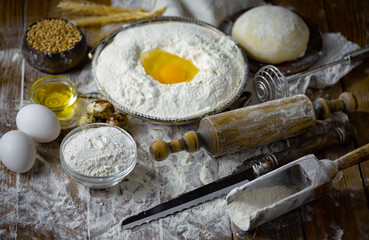 Kneading dough with flour and eggs, with kitchen accessories, on table and old background.