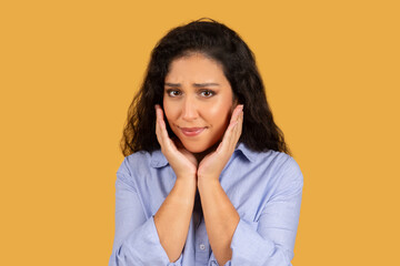 Worried young woman with curly hair holding her face in hands, looking