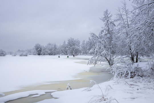 Photo of a winter landscape with snow-covered trees, bushes and a river. fishermen on winter fishing