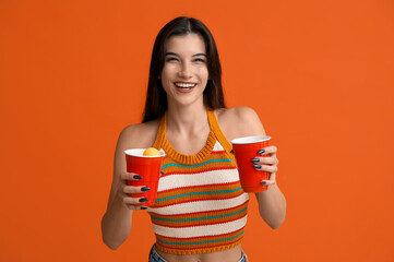 Beautiful young woman with plastic cups of cold beer on orange background