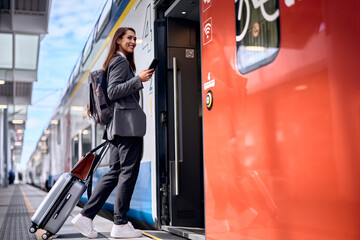 Happy woman using cell phone while getting into train at station.