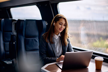 Smiling businesswoman works on laptop while commuting by train.