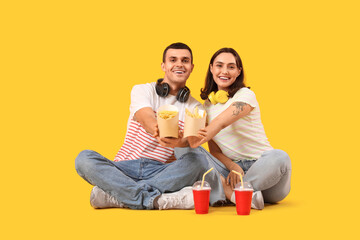 Young couple with french fries and cola on yellow background
