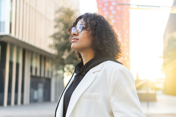 Confident young woman standing in city sunshine