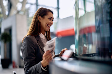 Cheerful woman buying travel ticket at train station. - obrazy, fototapety, plakaty