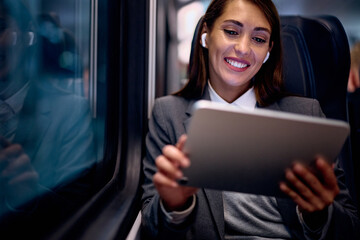 Happy businesswoman using earbuds and touchpad while commuting by train. - obrazy, fototapety, plakaty