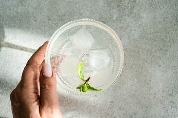 Refreshing drink with lime and mint in a glass held by hand