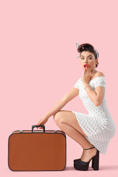 Shocked young pin-up woman with suitcase on pink background