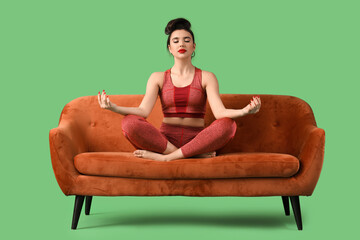 Sporty young pin-up woman meditating on sofa against green background
