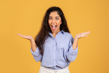 Excited young woman with long curly hair, dressed in a blue shirt, throws her hands up