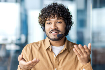 Web camera view, online video call, young man smiling and looking into camera with headset phone...