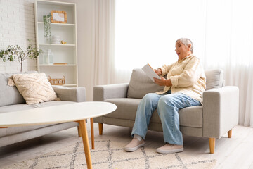 Senior woman reading book on sofa at home