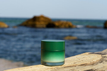 Fototapeta na wymiar Green mockup jar of cream on the background of sea water and stone illuminated by the daytime sun. Concept of natural beauty products with algae extract