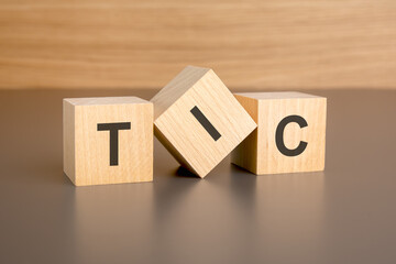 three wooden blocks on a brown background, with the abbreviation TIC - obrazy, fototapety, plakaty