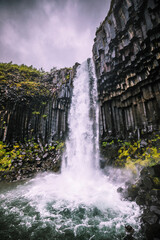 Thunderous masses of water cascade down the Skaftafell waterfall along gray basalt columns.