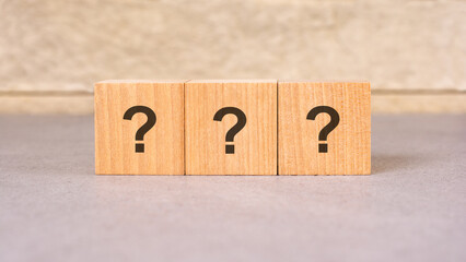 three wooden blocks with question marks over a grey background