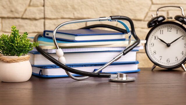 concept of studying medicine. stethoscope with a stack of books and a table clock in the background. training of doctors and medical students. High quality photo