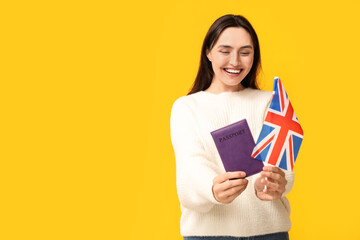 Pretty young woman with UK flag and passport on yellow background. Immigration concept