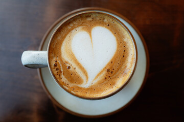 Heart shape in the froth of a flat white coffee in a cup and saucer on a dark wood table, seen from above. - 706723071