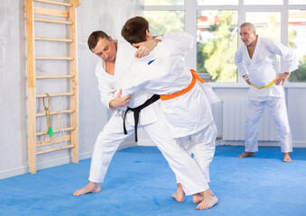 Adult man and young man judokas practicing judo fight in gym..
