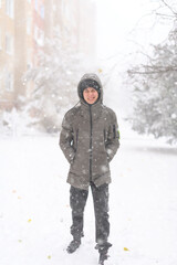 Fototapeta na wymiar A boy walks along a snowy street, it is snowing, blizzard and frost on a winter day