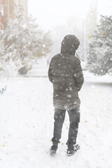 A boy walks along a snowy street, it is snowing, blizzard and frost on a winter day