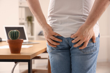 Young businessman with hemorrhoids in office, back view