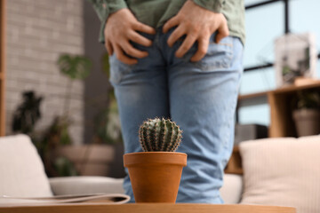 Cactus on table of young man with hemorrhoids at home, closeup