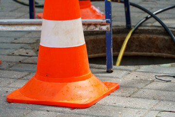 Orange cones installed around the dangerous area on the sidewalk. An open travel hatch. Laying of a new fiber-optic cable in the city network. orange construction cone
