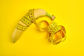 Measuring tape and banana on yellow background. Weight loss concept. Men's health concept. Top view, copy space