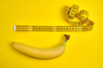 Measuring tape and banana on yellow background. Weight loss concept. Men's health concept. Top...