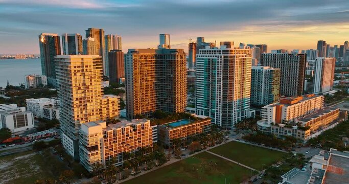 Bright orange light of setting sun on the facades of the high-rise buildings. Drone footage rising above the panorama on Miami Beach, Florida, USA at sunset.