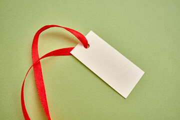 Brown cardboard label with red ribbon on a colored background. Tag for clothes, place for text.Eco...